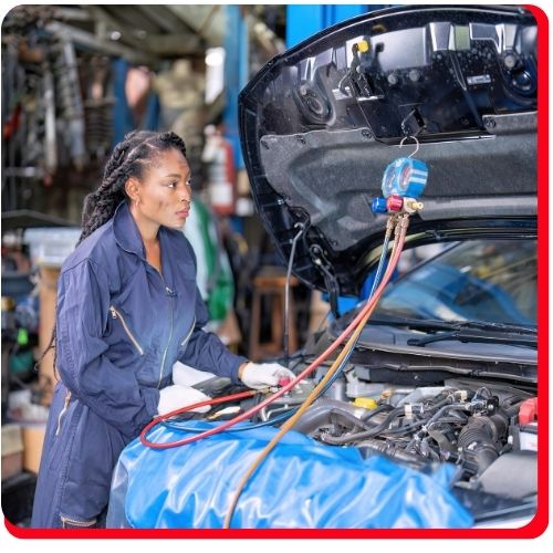 Female technician checking a car’s AC system with diagnostic gauges in an auto repair shop.