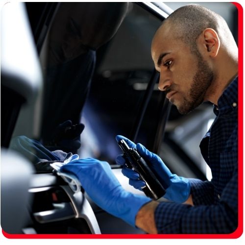 Technician wearing gloves cleaning and inspecting a car’s interior dashboard area.