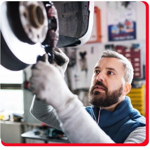 Mechanic performing a brake pad inspection and repair on a raised vehicle in a service garage.