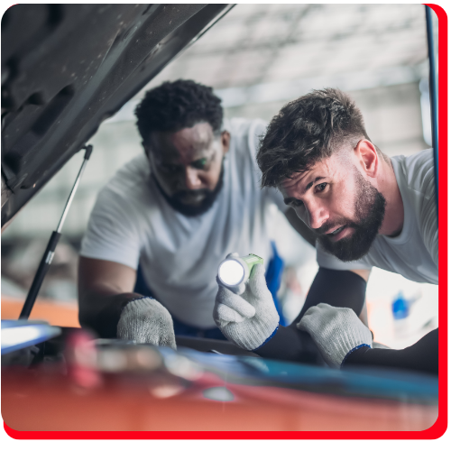 Two auto technicians using a flashlight to inspect a vehicle engine during car maintenance service.