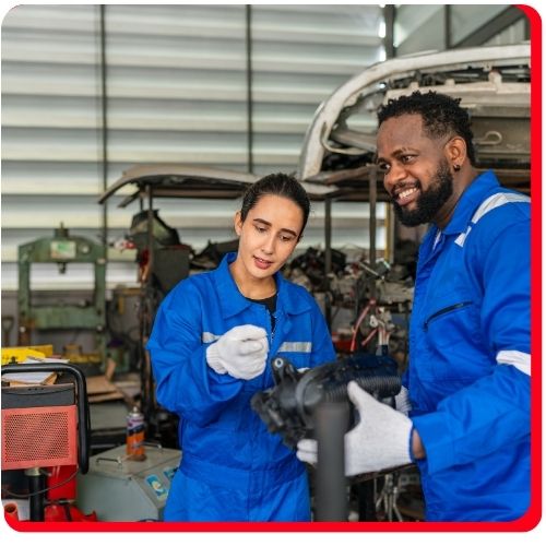 Two automotive technicians inspecting a CV axle part in a repair shop.