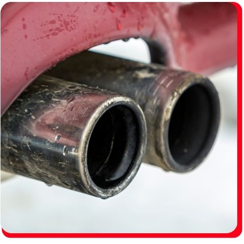 Close-up of corroded and dirty twin exhaust pipes on a red vehicle.