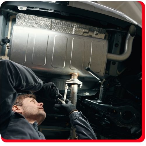 Mechanic tightening bolts on a car’s exhaust system from beneath the vehicle.