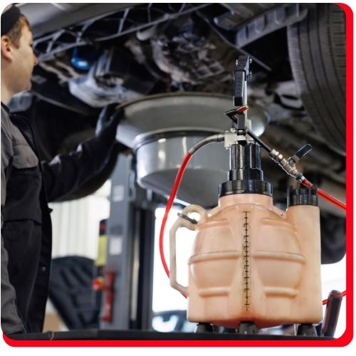 Mechanic performing an oil change using an advanced extraction system beneath a lifted vehicle.