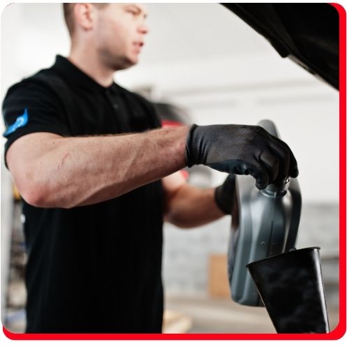 Auto technician pouring engine oil into a car during a routine oil change.
