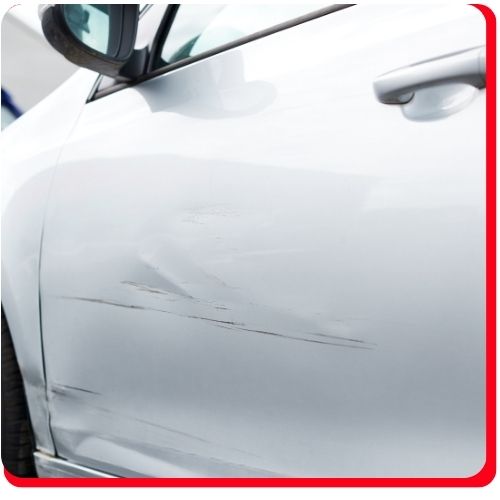 Scratches and minor dents on the front door panel of a white car.