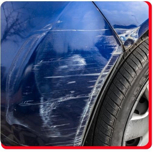 Heavy scratches and dents on the front fender of a blue car above the wheel.