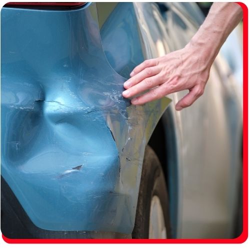 Hand inspecting a dented and scratched rear quarter panel on a blue vehicle.
