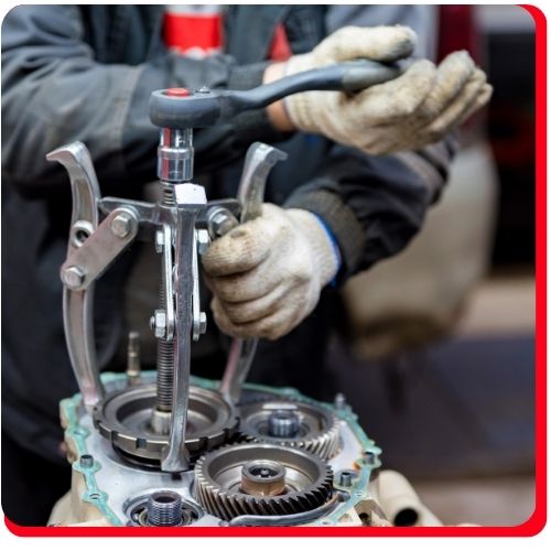 Mechanic using a gear puller tool during a manual transmission overhaul process.