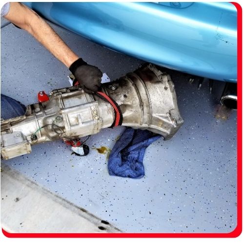 Auto technician removing a transmission from under a vehicle during overhaul service.