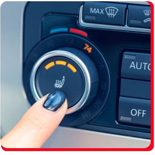 Finger pressing heated seat button on a car's air conditioning control panel.