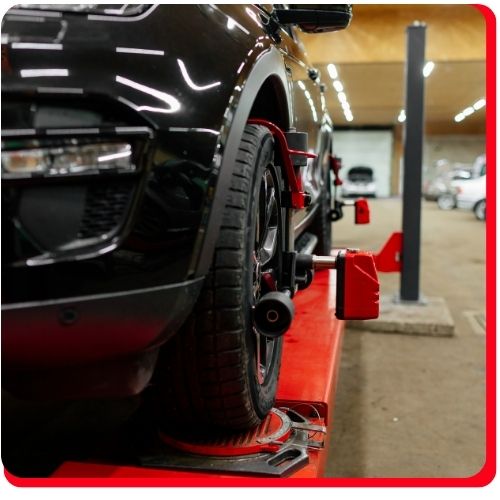 Black vehicle on a red lift undergoing digital wheel alignment at an auto service shop.