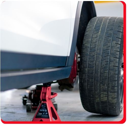 Car raised on jack stands with a detached wheel showing signs of uneven tire wear.