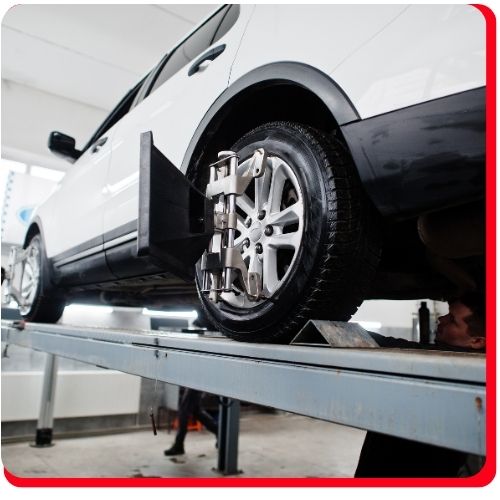 White SUV elevated on a lift with wheel alignment sensors attached.